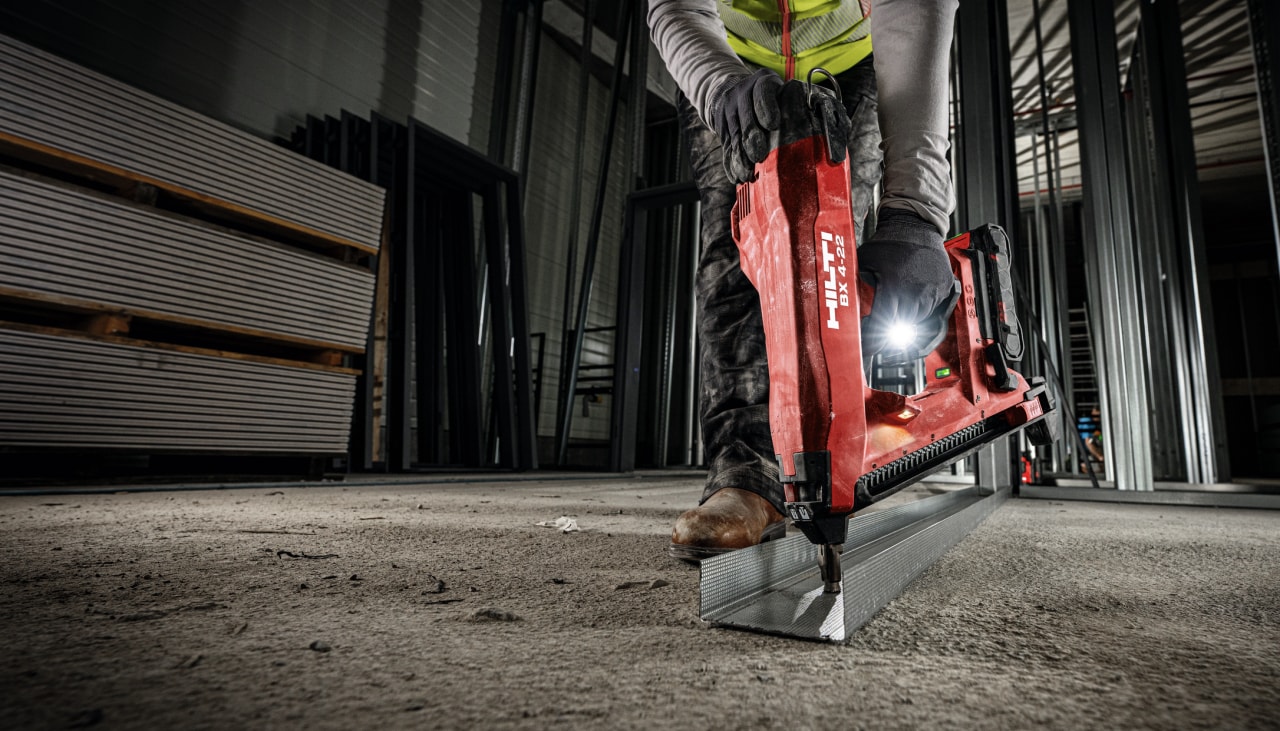 Worker fastening wooden track placopan on floor with BX 3